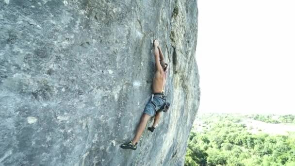 Młody silny muskularny opalony człowiek alpinista starannie wspina się na wysoki pionowy wapienny klif, próbując wisieć i spada — Wideo stockowe