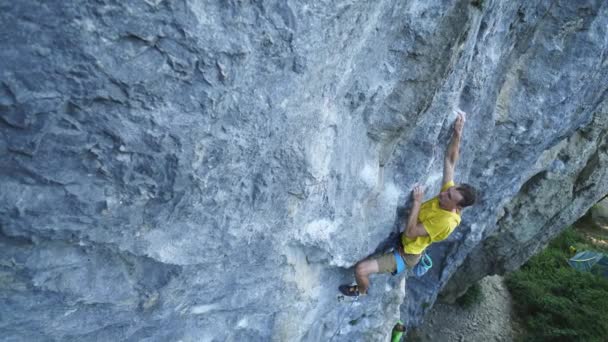 Vide hoek uitzicht op de mens rots klimmer, klimmen sport route op een klif, zoeken, bereiken en grijpen greep en knippen touw. — Stockvideo