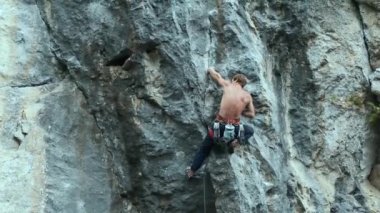 Arkaya bakan güçlü kaslı adam kaya tırmanışçısı dikey bir uçurumda spor rotasına tırmanıyor.
