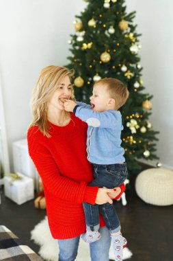 Kırmızı kazaklı çekici bir kadın oğlunu kucağında tutuyor. Küçük bir çocuk annesine Noel kurabiyesi yediriyor. Arka planda Noel ağacı var..