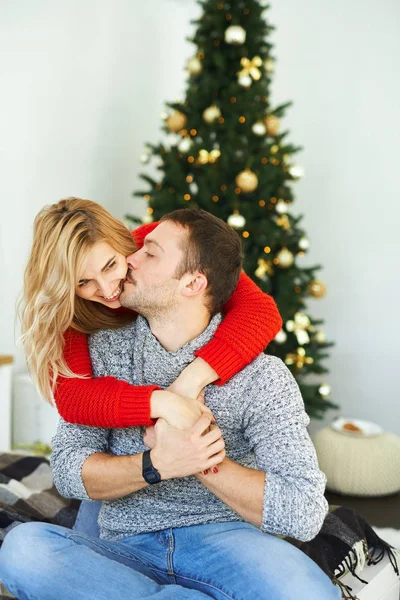 Pareja romántica enamorada abrazándose, besándose sentada, en la cama cerca del árbol de Navidad en casa . —  Fotos de Stock