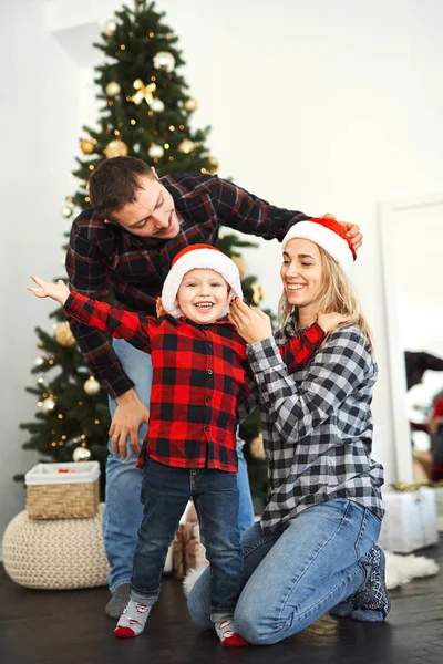 Julefamilie. Far, mor og sønn i julenissehatter tilbringer tid sammen nær juletreet hjemme . – stockfoto