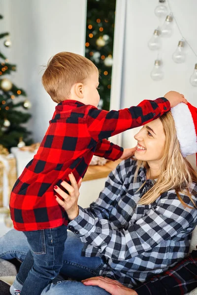 En liten gutt tar på seg en julenisse-hatt til mamma . – stockfoto