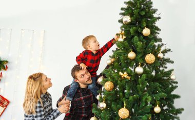 Noel arifesinde Noel ağacı süsleyen genç bir aile..