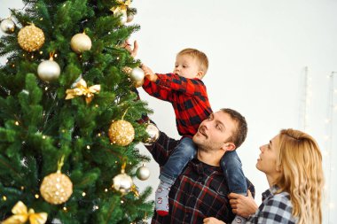 Noel arifesinde Noel ağacı süsleyen genç bir aile..