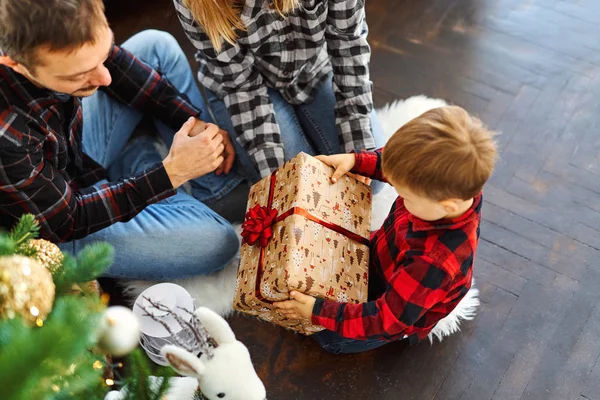 Nuori perhe juhlii joulua kotona, istuu kauniin joulukuusen lähellä, nauraa, syleilee ja antaa lahjoja — kuvapankkivalokuva