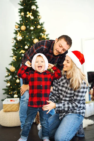 Julefamilie. Far, mor og sønn i julenissehatter tilbringer tid sammen nær juletreet hjemme . – stockfoto