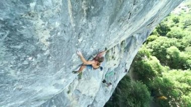 Genç güçlü kaya tırmanışçısı dikey kireç taşı uçurumuna tırmanıyor, halatı bağlıyor ve bitiş rotasını tamamlıyor.