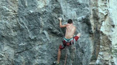 Arkaya bakan genç kaslı adam kaya tırmanışçısı zorlu bir spor rotasına tırmanıyor dikey bir uçurumda