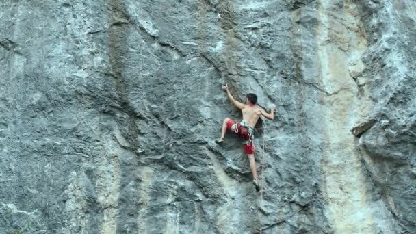 Hombre musculoso escalador de roca de cámara lenta escalando cuidadosamente en un alto acantilado de piedra caliza vertical — Vídeos de Stock