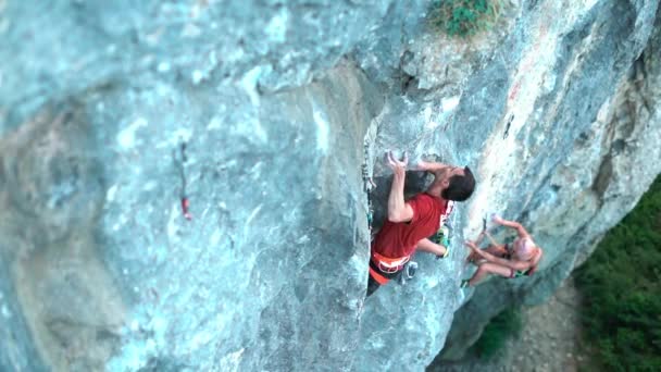 Top view paar rotsklimmers klimmen op stoere sport routes, man bereiken hold op de voorgrond, vrouw klimt op de achtergrond. — Stockvideo