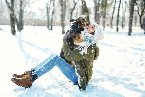 Mladá šťastná žena ve vlněném klobouku a dlouhou teplou šálu drží svého mazlíčka ve sněhobílém zimním parku v zamrzlém slunečném dni — Stock fotografie