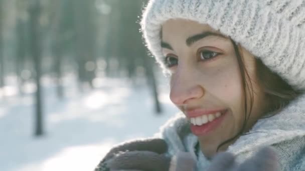 Extreme closeup πορτρέτο της όμορφης χαμογελαστή γυναίκα σε μάλλινο καπέλο και μακρύ ζεστό κασκόλ σε χιονισμένο χειμερινό πάρκο σε αφρώδη ηλιόλουστη μέρα — Αρχείο Βίντεο