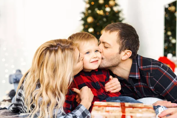 Genç ebeveynler oğullarını öpüyor ve Noel 'de küçük bir çocuğa hediye veriyor..