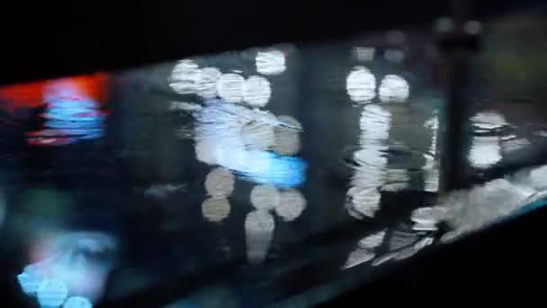 Gros plan gouttes de pluie tombant sur flaque d'eau avec réflexion des lumières sur le trottoir de la ville . — Video