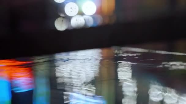 Slow motion closeup Rain drops Falling On puddle with lights reflection on city sidewalk. — Stock Video