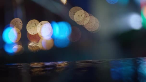 Slow motion closeup Rain drops Falling On puddle with lights reflection on city sidewalk. — Stock Video