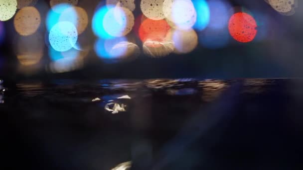 Slow motion closeup Rain drops Falling On puddle with lights reflection on city sidewalk. — Stock Video