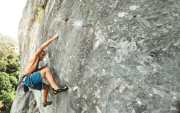 Starker muskulöser Mann Felskletterer mit nacktem Oberkörper, der dynamisch an einer senkrechten Klippe klettert, — Stockfoto