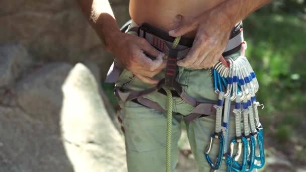 Hombre irreconocible escalador de roca con torso desnudo preparándose para escalar al aire libre en el acantilado, y atar la cuerda al arnés de escalada — Vídeos de Stock