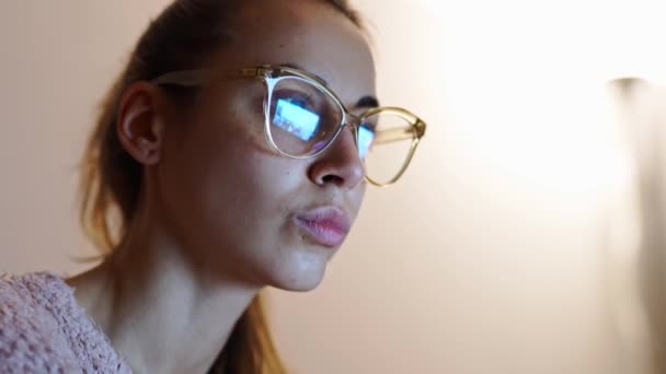Молода жінка фрілансер в окулярах сидить на самоті вночі працює і використовує ноутбук, дивлячись на монітор — стокове відео