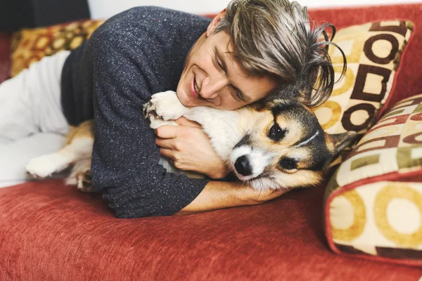 Portrait of young man embracing his pet. Cute Welsh Corgi puppy resting with owner, spending time together at home. — Stock Photo, Image