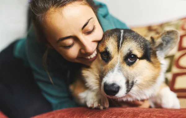 Retrato de jovem mulher sorridente abraçando animal de estimação. Bonito cachorro galês Corgi descansando com o proprietário, passando tempo juntos em casa . — Fotografia de Stock