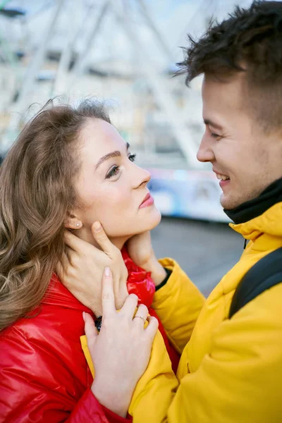 Mutlu genç çift, birbirlerine gülümseyip sarılıyorlar, açık sarı ve kırmızı ceketler giyiyorlar.. — Stok fotoğraf