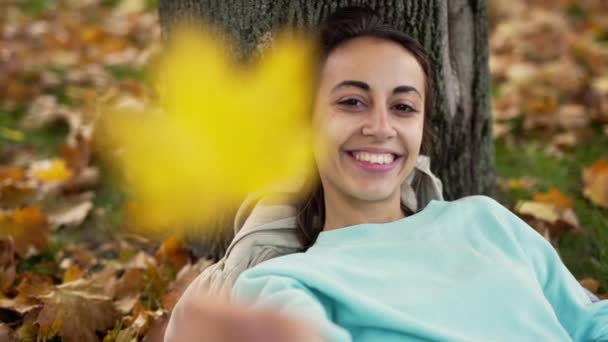 Top uitzicht op mooie jonge vrolijk glimlachende vrouw spelen met fel oranje blad in het najaar park. — Stockvideo