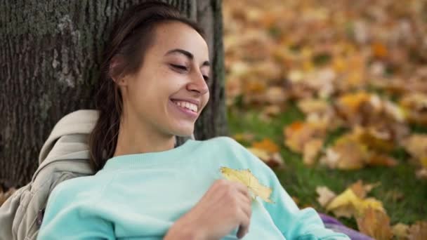 Top view of beautiful young cheerfully smiling woman playing with bright orange leaf in the autumn park.. — Video
