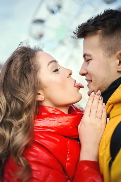Rolig ung kvinna i röd dunjacka sticker tungan ut, visar roliga ansikten för sin pojkvän. — Stockfoto