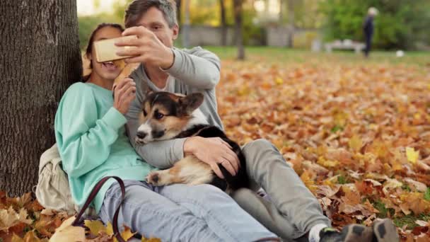 Iubitor Cuplu de a face selfie pe smartphone cu tricolor drăguț Welsh Corgi Dog In City Park îmbrățișare relaxant bucurându-se de o zi caldă în aer liber — Videoclip de stoc