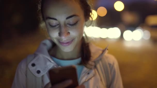 Close-up van de prooi lachende vrouw met behulp van smartphone lopen 's nachts stad — Stockvideo