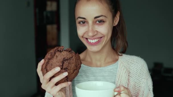 Щаслива усміхнена жінка позує з великим шоколадним печивом і великим чашковим чаєм — стокове відео