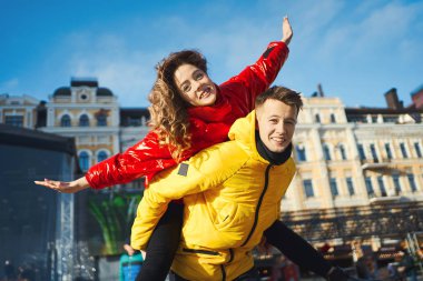 Güneşli bir günde şehirde yürüyen ve birlikte eğlenen genç bir çiftin portresi. Genç adam kız arkadaşını omuzlarında taşıyor..