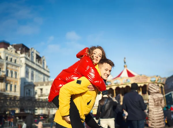 Felice giovane coppia che cammina per la strada della città in giorno di sole luminoso, divertirsi insieme. giovane uomo che porta la sua fidanzata sulle spalle. — Foto Stock