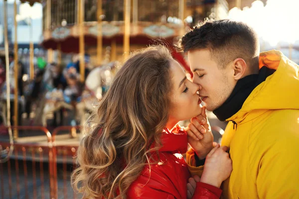 Close-up retrato jovem romântico casal apaixonado abraçando e beijando no fundo carrossel francês. — Fotografia de Stock