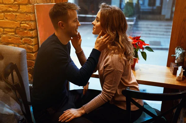 Tânăr bărbat și femeie îmbrățișează și se atinge reciproc într-o cafenea confortabilă în fața ferestrei mari . — Fotografie, imagine de stoc