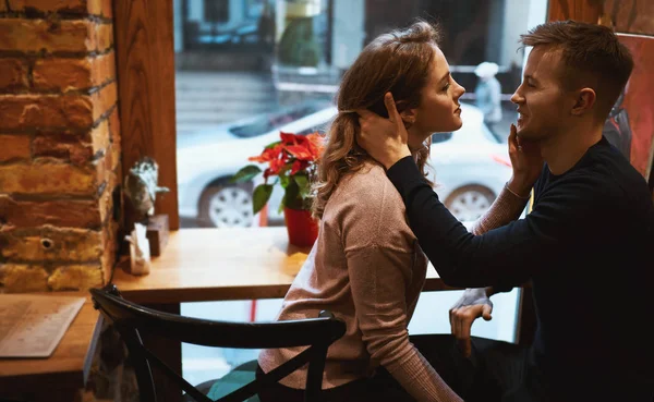 Ung man och kvinna ömt kramar och rör varandra i mysiga café framför stora fönster. — Stockfoto