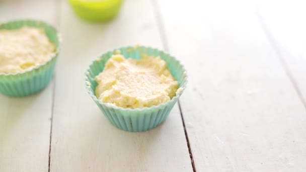 Mehrere kleine Silikonformen zum Backen mit rohem Teig für Käsekuchen auf weißem Holztisch — Stockvideo