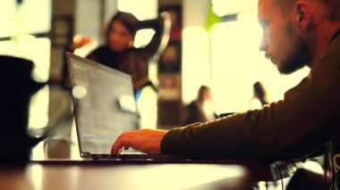 Adam kafede oturmuş laptopta çalışıyor.