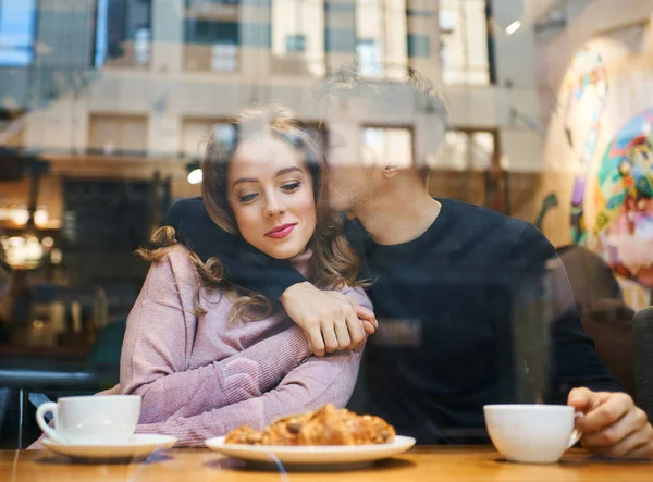 Glada romantiska par sitter över fönstret i caféet, omfamnar, kysser och dricker kaffe. pojkvän ömt kramar och kysser flickvän i mysiga café. — Stockfoto