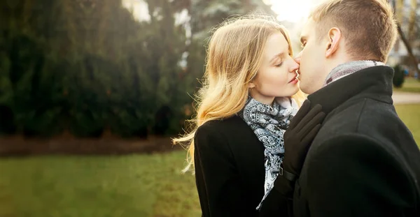 Retrato de bela mulher elegante em casaco preto beijando homem com olhos fechados — Fotografia de Stock
