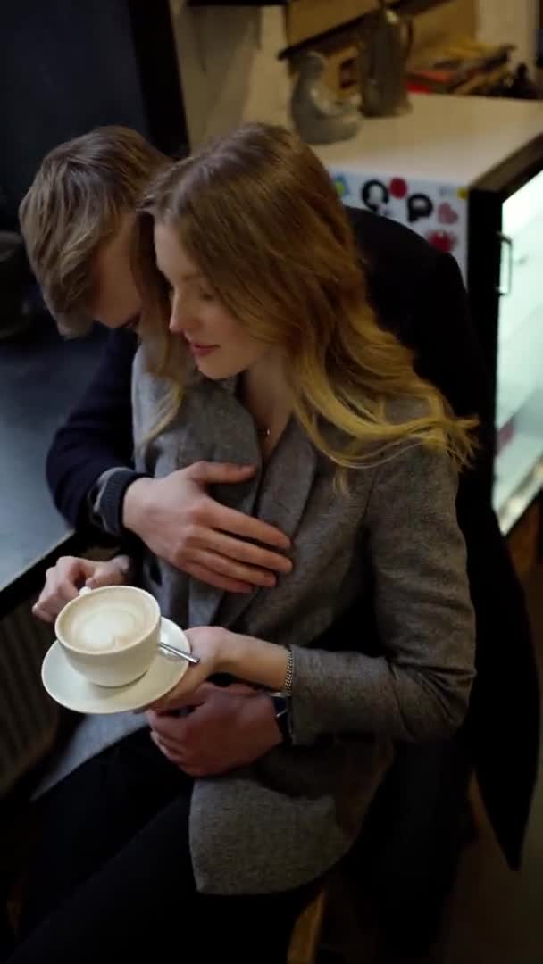 Filmación vertical para dispositivos móviles pareja en una cita en acogedora cafetería, hablar, beber café de una taza y divertirse juntos — Vídeos de Stock