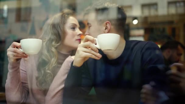 Young Happy romantic couple sitting over the window in cafe, embracing, kissing and drinking coffee — Stock Video