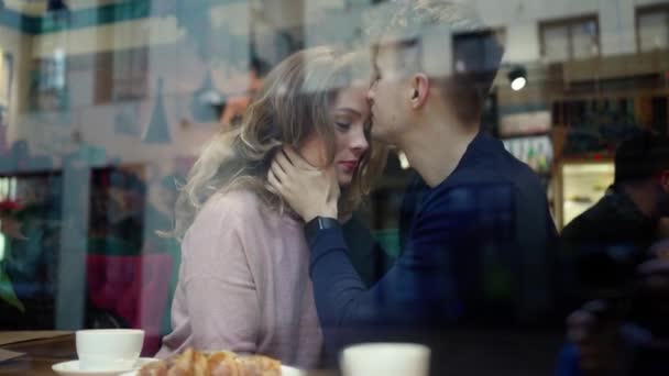 Niedlich Glückliches romantisches Paar umarmt und küsst sich, während es über dem Fenster im Café sitzt. junger Mann umarmt und küsst Freundin in gemütlichem Café — Stockvideo