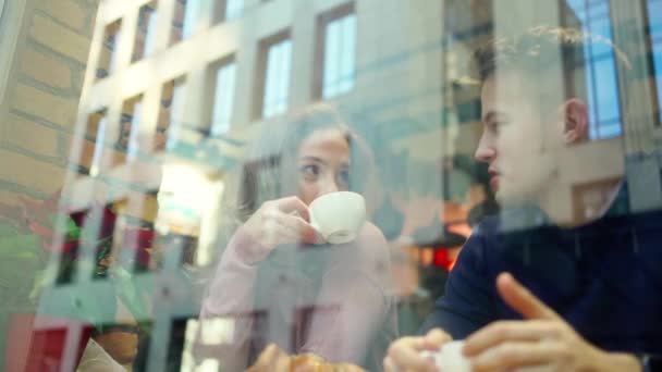 Joven hermosa pareja hombre y mujer en una cita en acogedora cafetería, hablar, beber café y divertirse juntos . — Vídeos de Stock