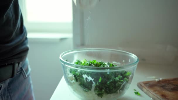 Man cooking vegeterian salad. close up man adding salt in glass bowl with cutted cabbage and green herbs — Stock Video