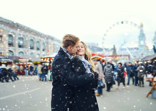 Elegante pareja romántica en el amor abrazando y besando en la calle en el día de nieve con atracción en segundo plano.. —  Fotos de Stock