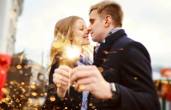 Elegante pareja romántica con espolvorear en abrazos de manos y besos en las decoraciones festivas de la ciudad de fondo.. —  Fotos de Stock